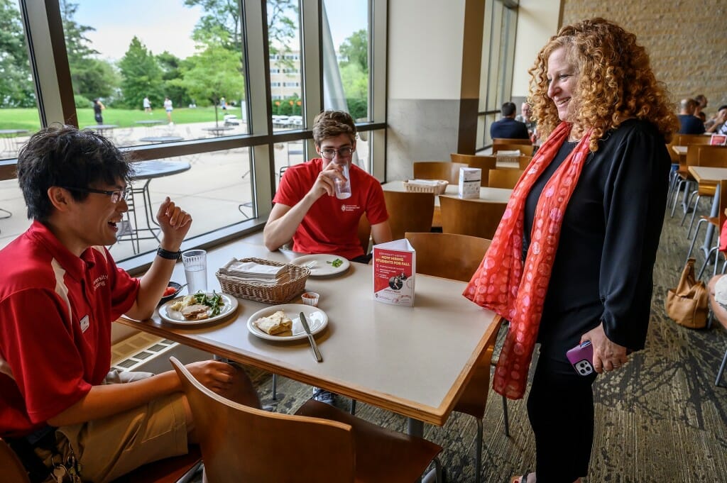 At right, Chancellor Mnookin visits with upperclassmen Bill Zhu (left) and Henry Wysong-Grass (center) as they eat lunch outside of Four Lakes Market in the Dejope Residence Hall.