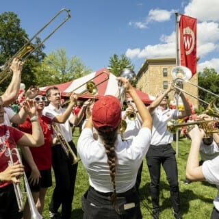 Band members lift their instruments high in the air as they play in the sunshine on the lawn of Bascom Hill.