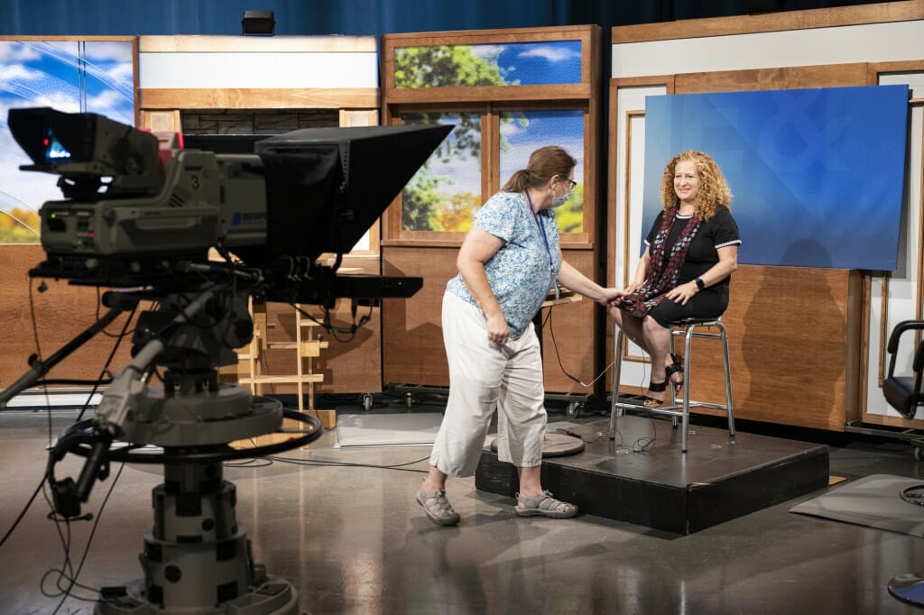A technician checks the mic on Jennifer Mnookin as she sits in a chair on a television news set.