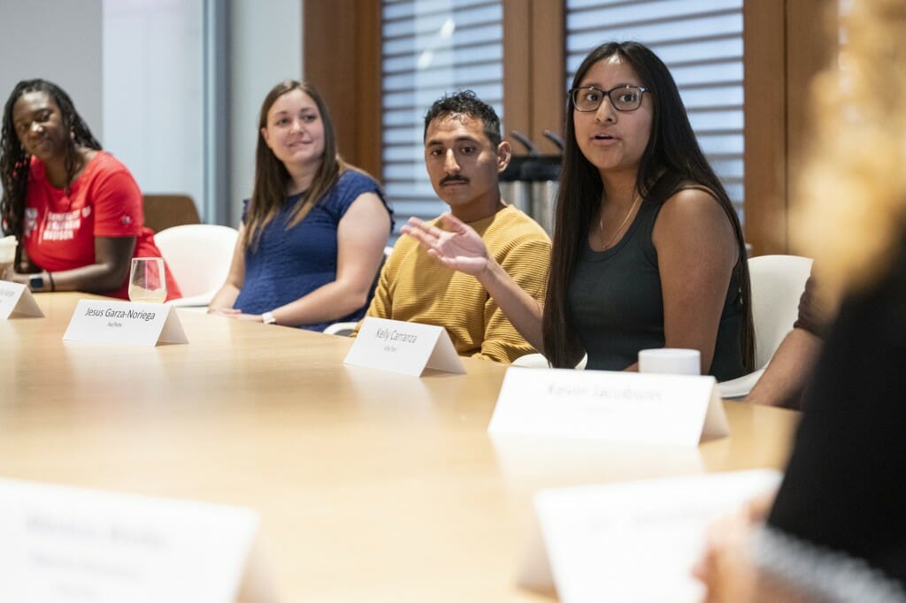 A student sitting at a table with others gestures as she talks.