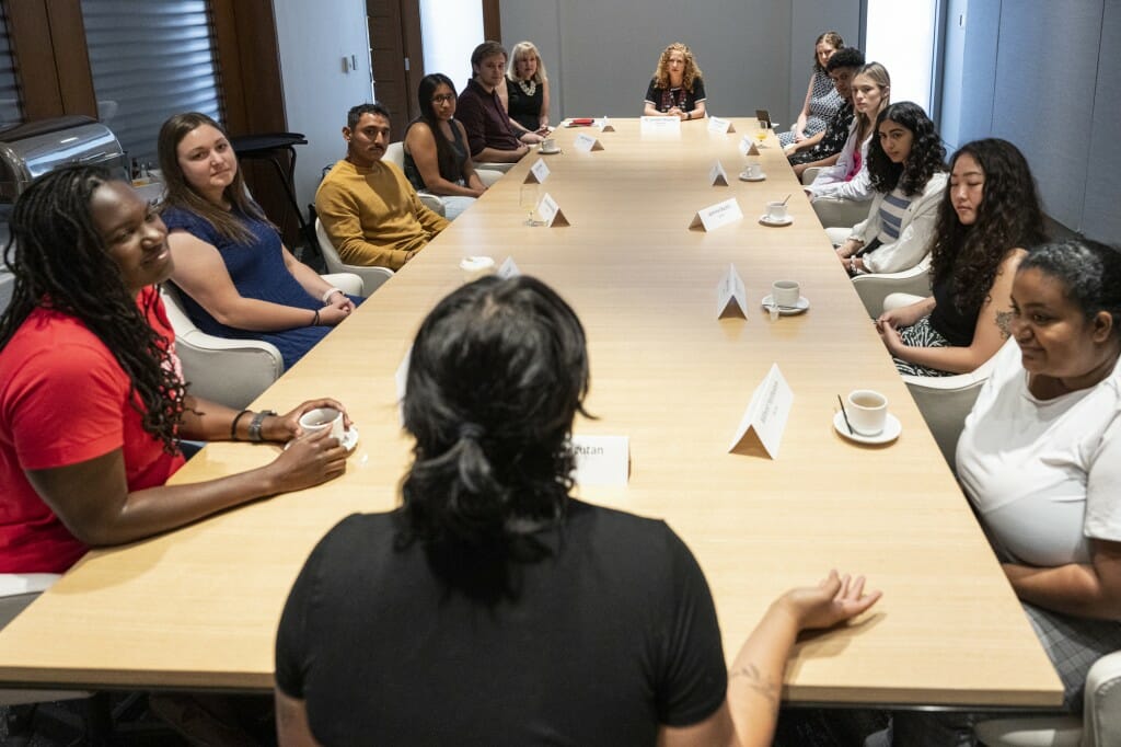 Chancellor Mnookin sits at the head of a table lined with students; one of the students is talking.