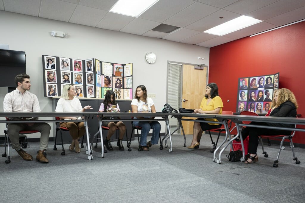 Chancellor Mnookin sits at a table while listening to UW-Madison students interns speaking