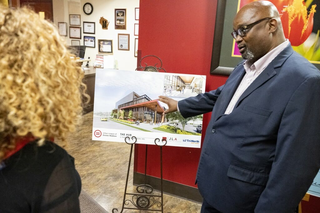 A man and woman stand in front of a poster showing building plans