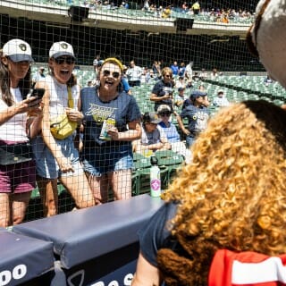 Chancellor Mnookin wears a navy blue Brewers shirt and poses with Buck Badger in front of a group of Brewers fans