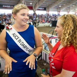 Chancellor Mnookin wears a red shirt as she talks to a young woman who wears a blue dress and a white sash