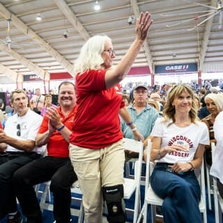A woman wears a red polo shirt and stands up to give a wave to the surrounding crowd