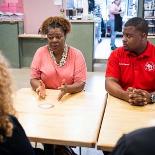 A woman in a pink shirt sits next to a man in a red shirt across a table from UW-Madison Chancellor Mnookin, who wears a black shirt