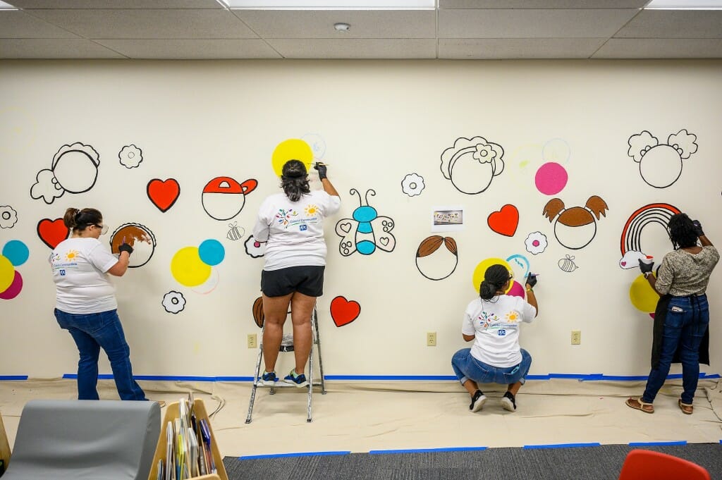 Four people apply paint to an intricate mural design on a wall.