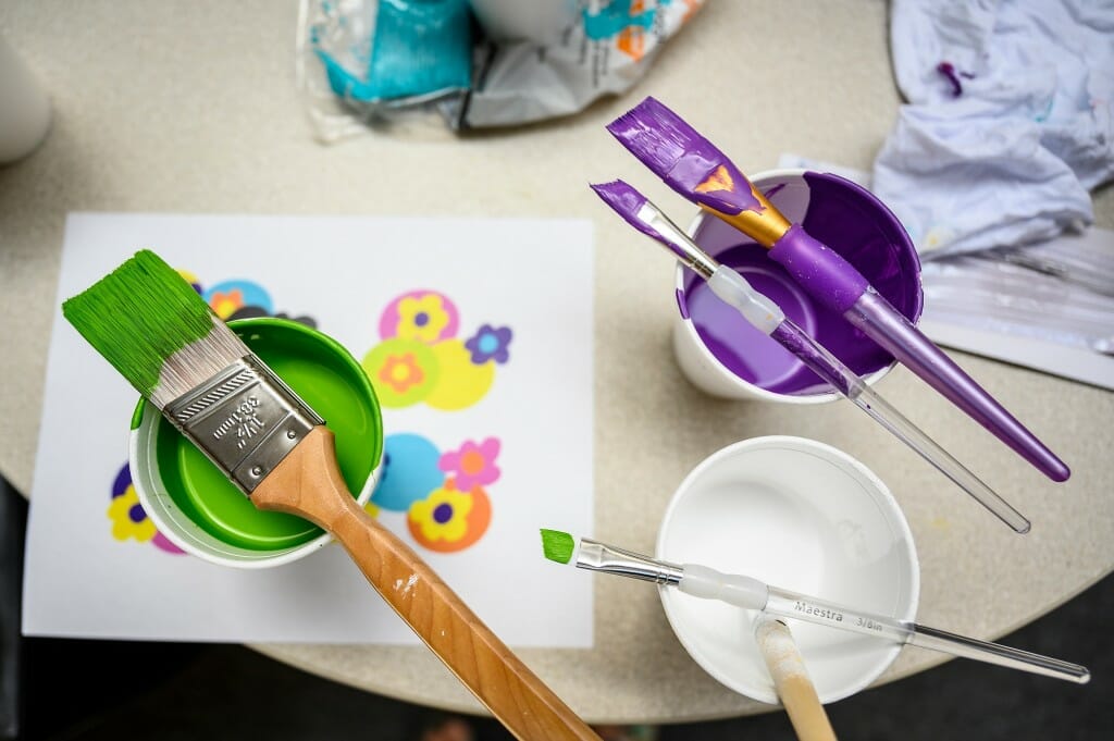 Paint brushes sit on cans of brightly colored paint.