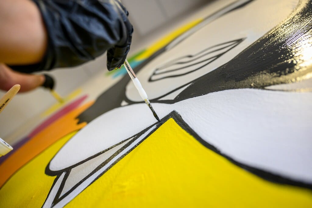 A close-up of a paint brush applying paint to the mural.