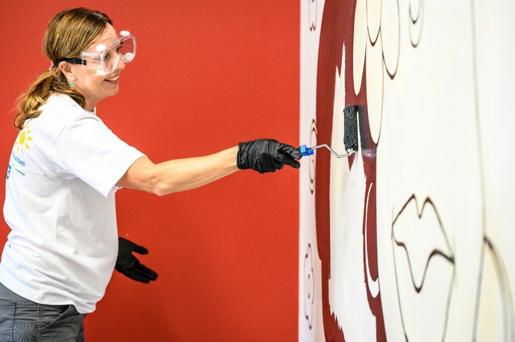 A woman holds a paint roller and paints a wall.