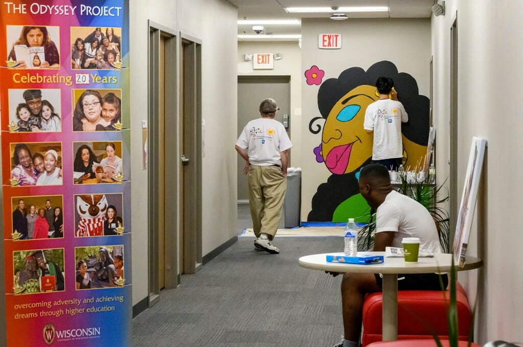 A mural is pictured at the end of a hallway, with two people looking at it.