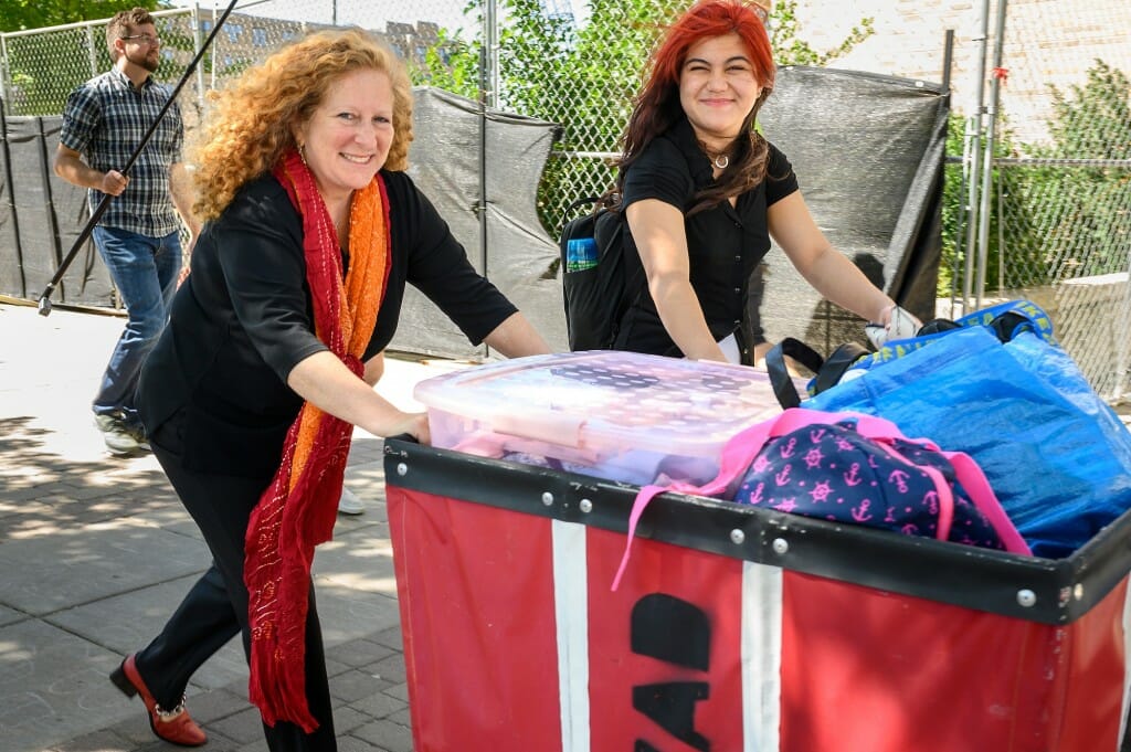 Chancellor Mnookin helps another women push a red cart filled with belongings.