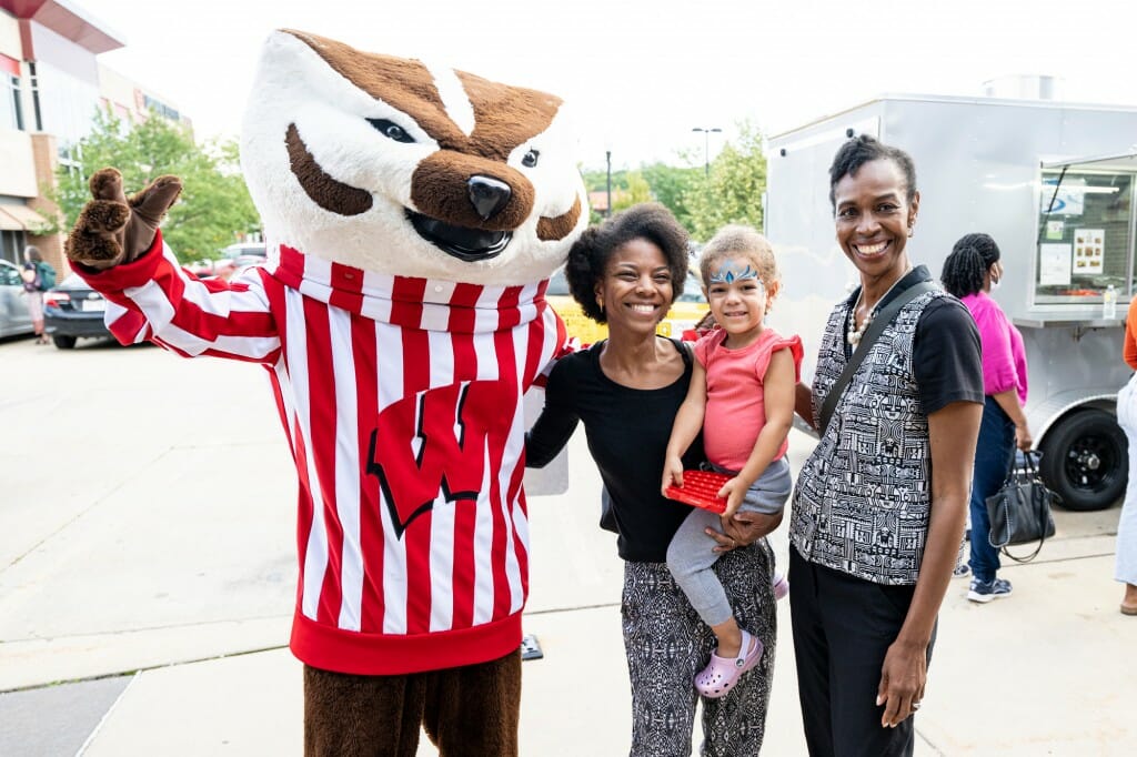 Two adults and a child pose for a photo with Bucky Badger.