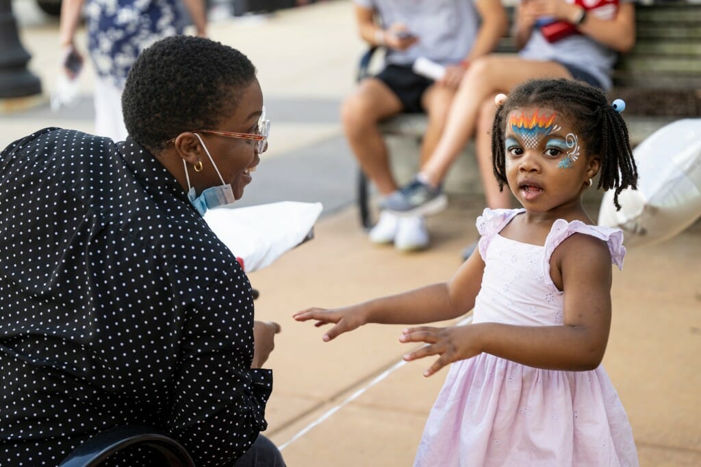 A girl with face paint on talks to a woman.