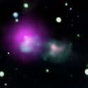 telescope image of blurry stars in space around a magenta blob next to a pink smudge within a greenish cloud