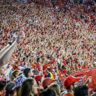 A mass of fans wearing red and white raise their arms and yell.