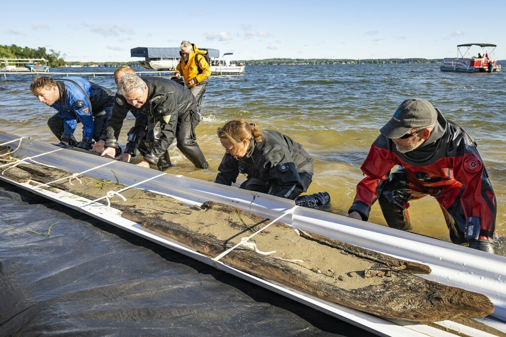 Jim Skibo, Wisconsin state archaeologist (center), and members of the dive team lift a makeshift raft holding the canoe onshore.