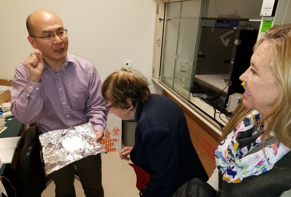 Wan-Ju Li holds up a sample of collagen fiber on a piece of foil. Gwen and Karen Plunkett stand right looking at the sample.