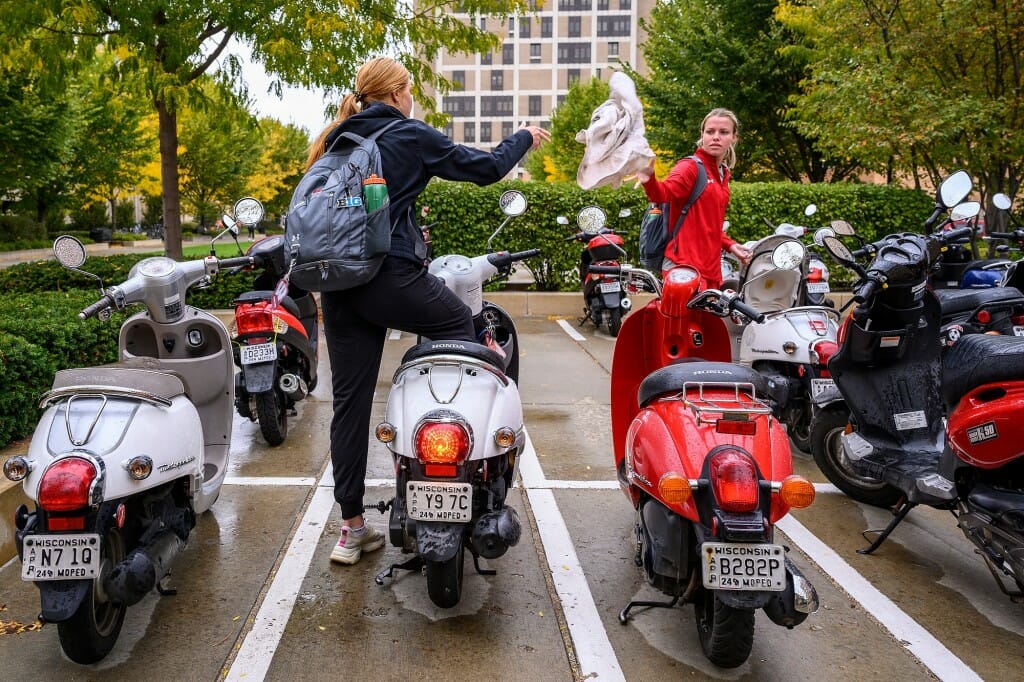 Two women high five as they stand over their parked scooters.