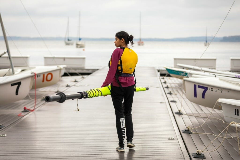 Engineering student Alisha Handa stands on a dock at the Memorial Union holding a wrapped neon sail on a rainy day.