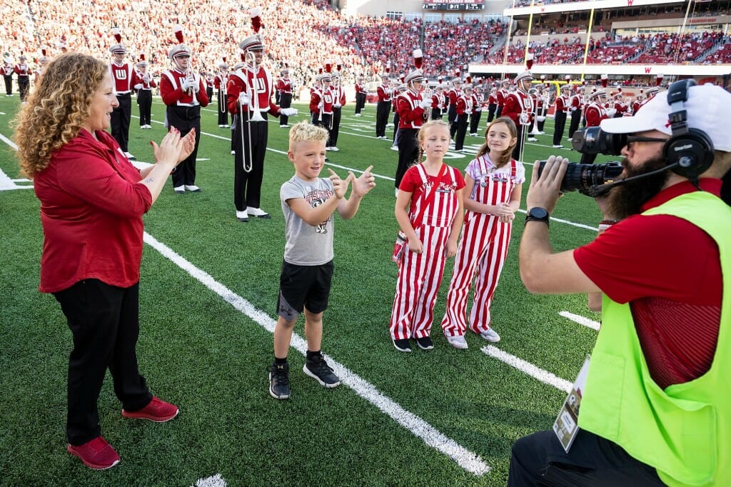 UW–Madison Chancellor Jennifer Mnookin, left, applauds as mini marshals are introduced on the video scoreboard during halftime.