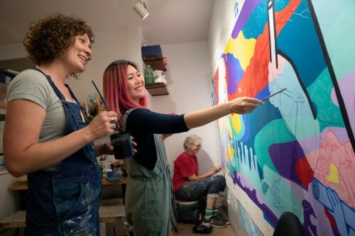 From left, artists Amy Zaremba, Sharon Tang, and Alicia Rheal work on a science-oriented mural