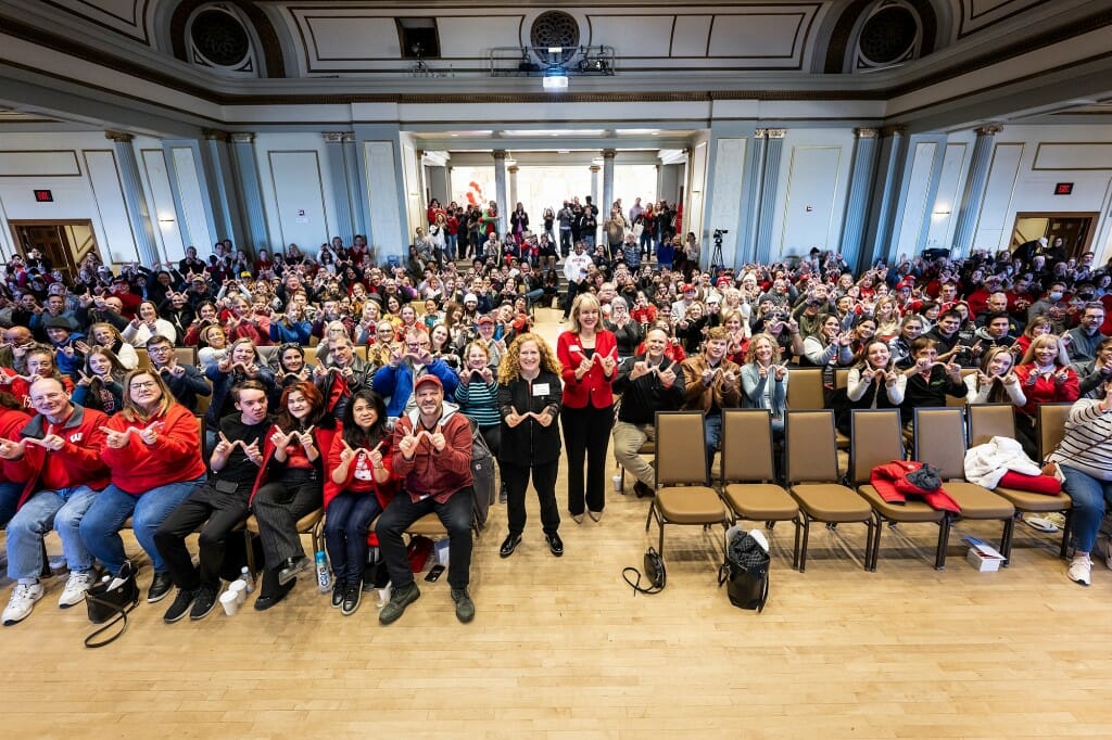 At center, Chancellor Jennifer Mnookin and Lori Reesor, vice chancellor of student affairs, throw up W hand signs with an audience of nearly 500 people, many of them parents of UW students.