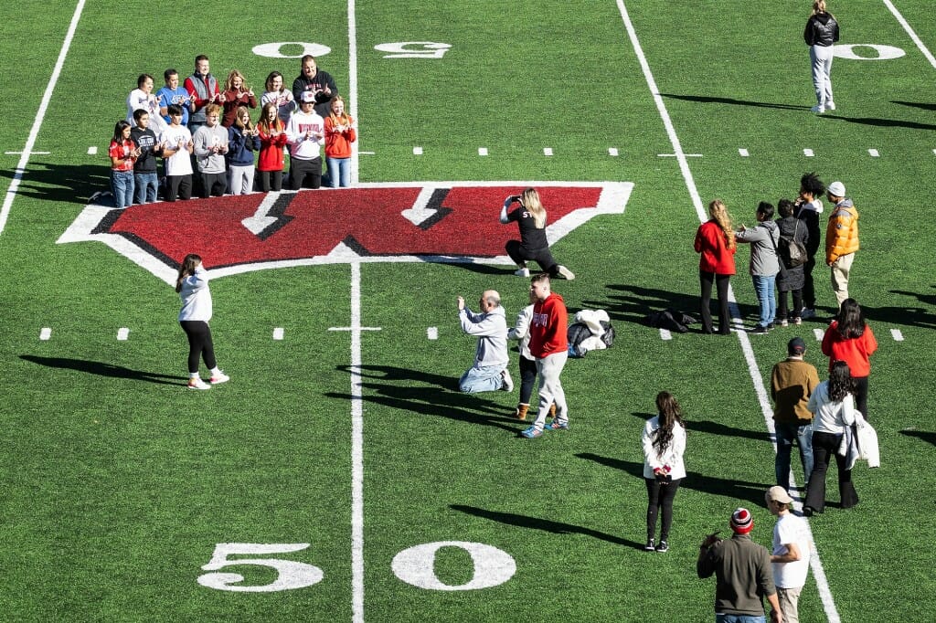 Family Weekend participants pose for photos near the Motion W logo on the football field at Camp Randall Stadium.