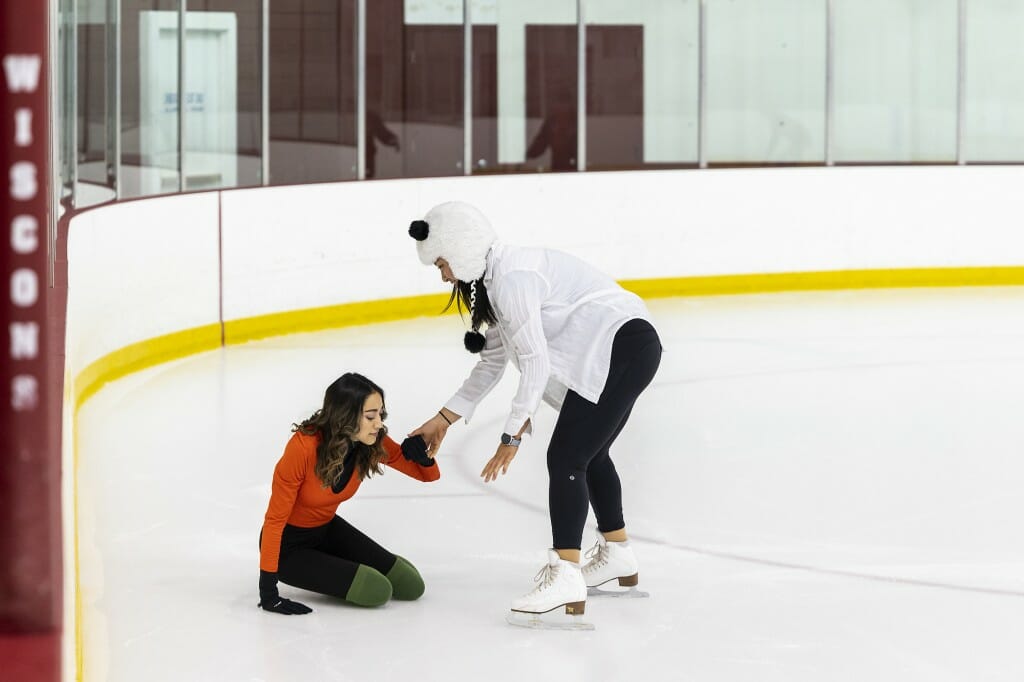 A woman helps another woman who's kneeling on the ice.