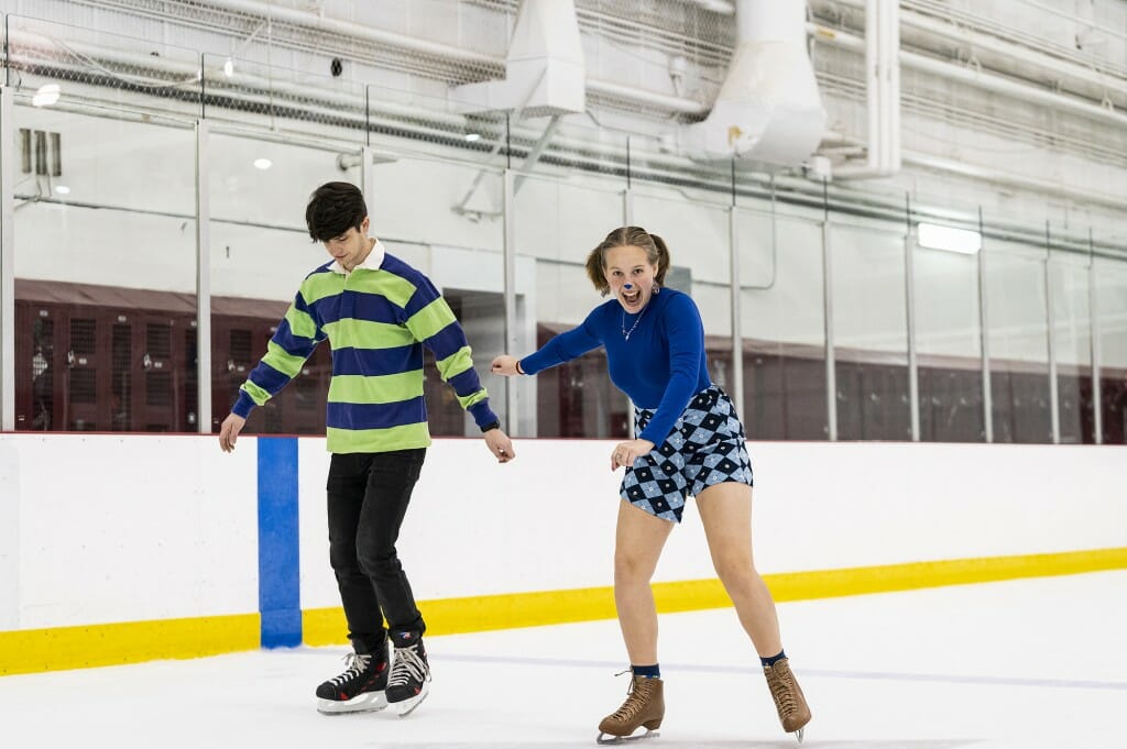 A man in a striped sweater and a woman in blue skate on a rink.