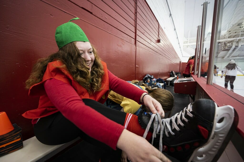 A person in a red costume ties her skates while sitting on a bench.