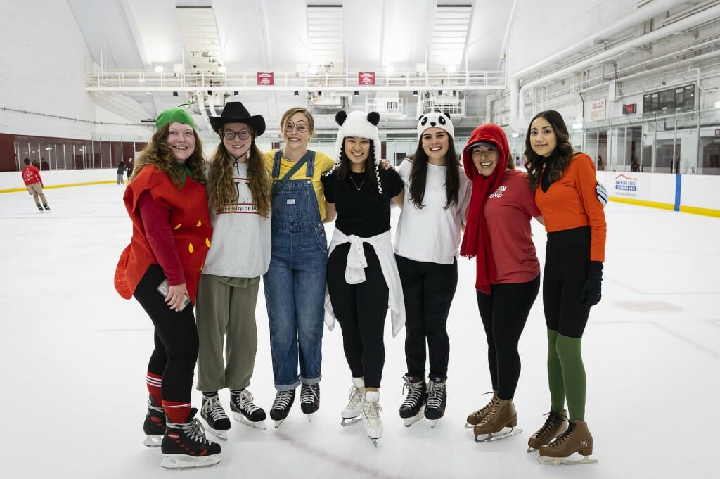 Seven people on ice skates stand arm in arm.