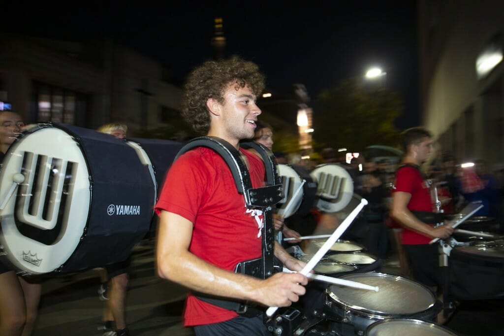 A UW Band member plays the drums as floats and performers travel down State Street before a crowd of spectators.