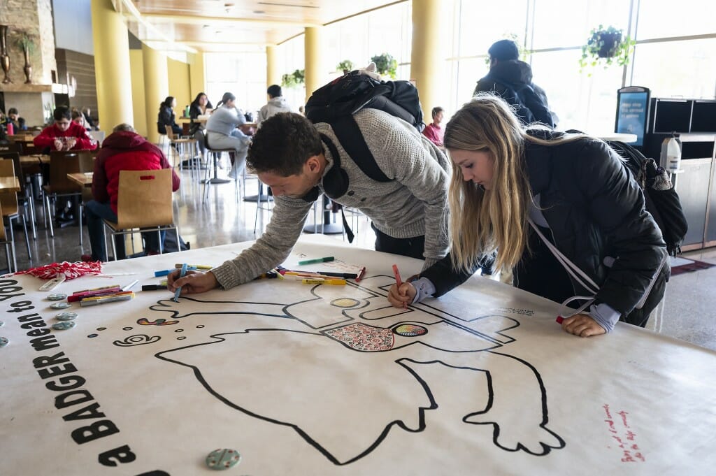 Students draw on a mural.