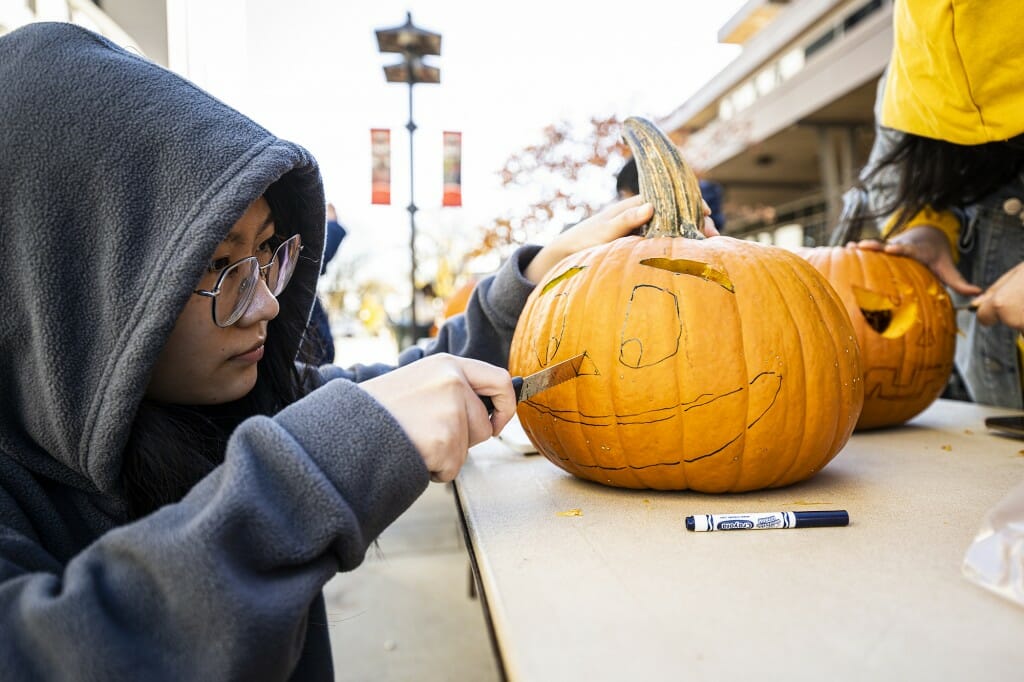 A person carefully carves out a face that's been inked on a pumpkin.