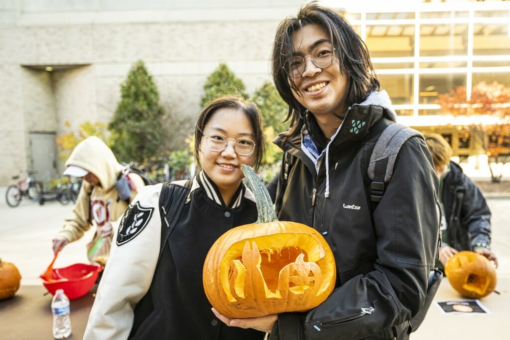 Two people hold a carved pumpkin and smile at the camera.