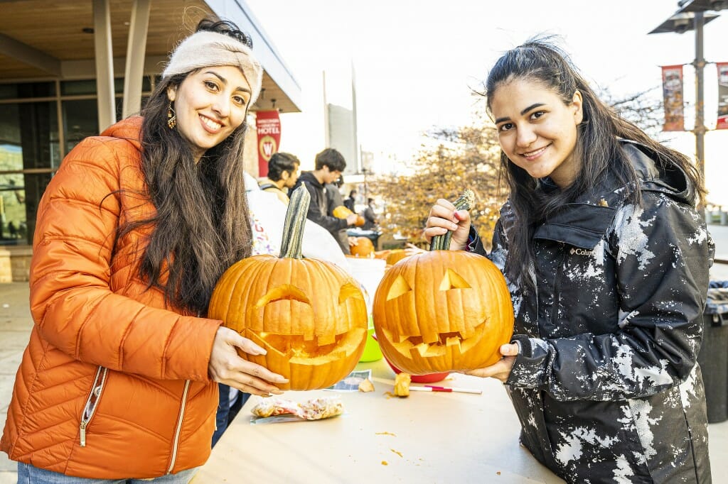 Students Neda Karami-Mohammadi (left) and Negin Sheybani show off their finished products, their own smiles matching the pumpkins'.