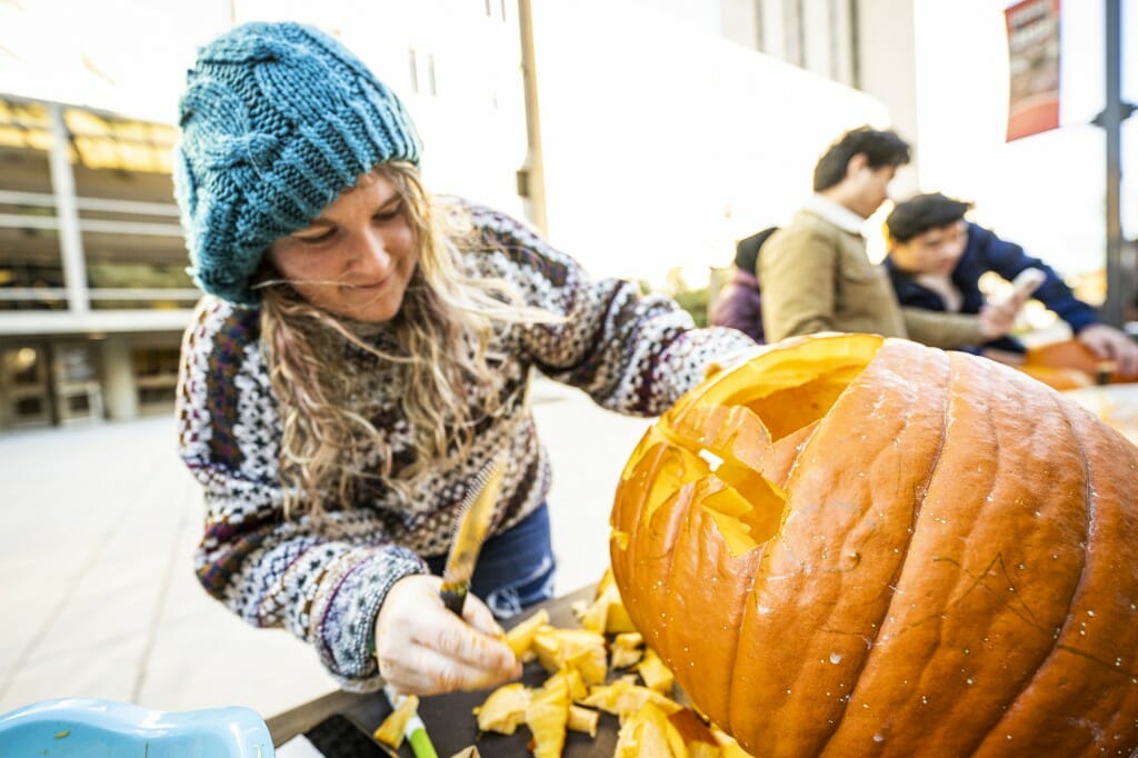A woman with knife carves out a pumpkin's mouth.