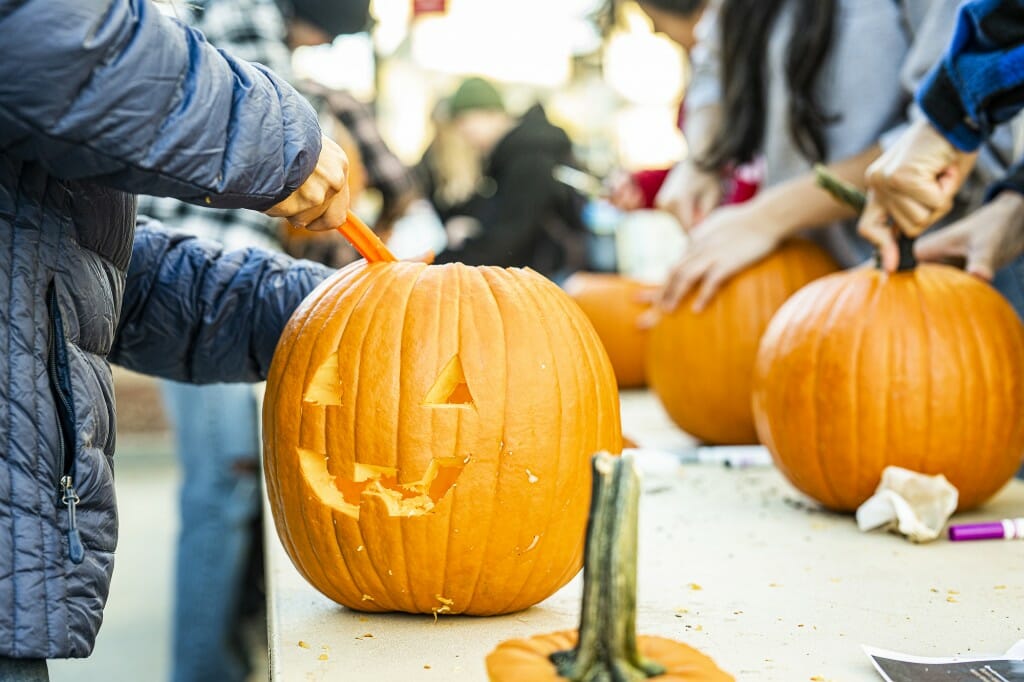 A person with a big spoon scoops out the innards of a carved pumpkin.