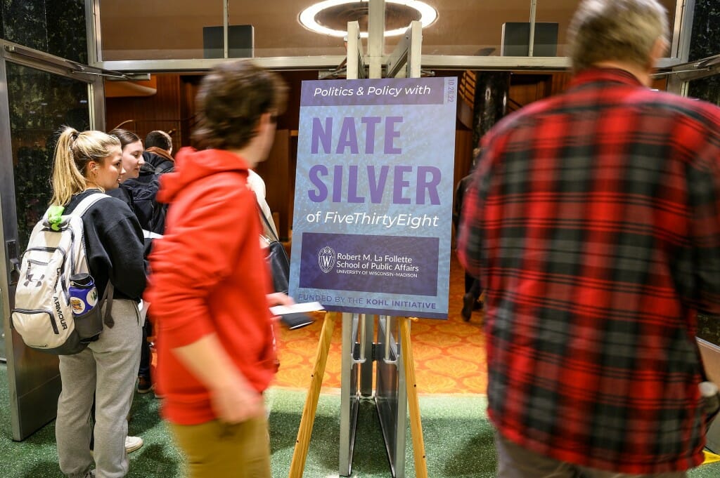 Audience members enter Shannon Hall in the Wisconsin Union Theater, passing a sign promoting the event.