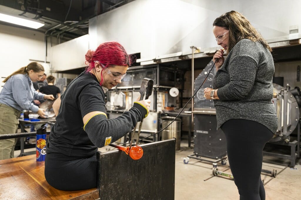 Two people work together on glass blowing.