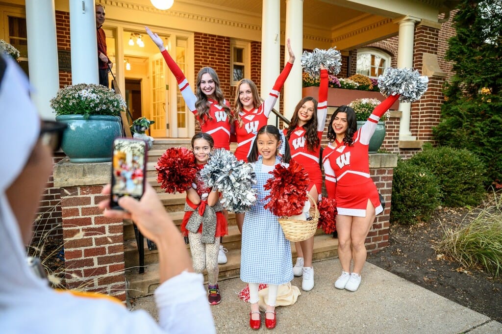 A young trick-or-treater dressed as Dorothy from the Wizard of Oz poses with members of the UW Spirit Squad on the steps of Olin House.