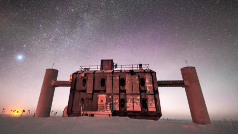 Front view of the IceCube Lab at twilight, with a starry sky showing a glimpse of the Milky Way overhead and sunlight lingering on the horizon.