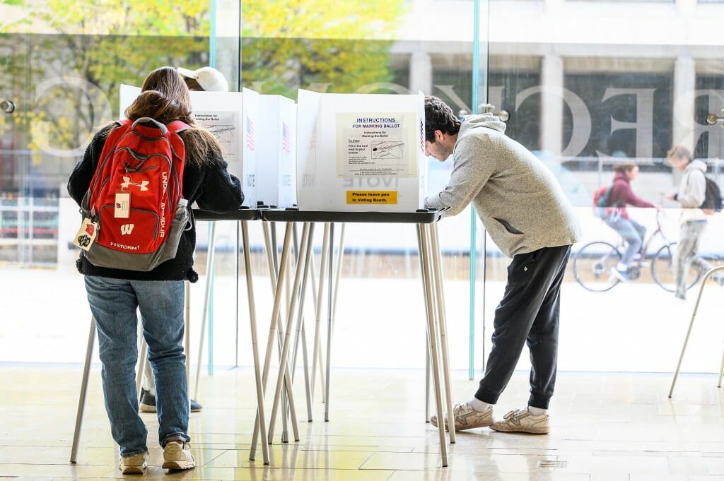 Students fill out midterm election ballots while pedestrians and bikers pass by outside of the Chazen Museum of Art