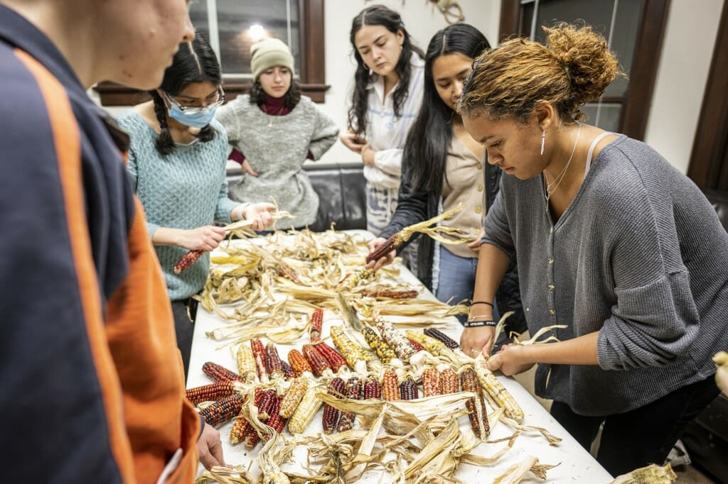 Several students stand around a table, braiding white corn.