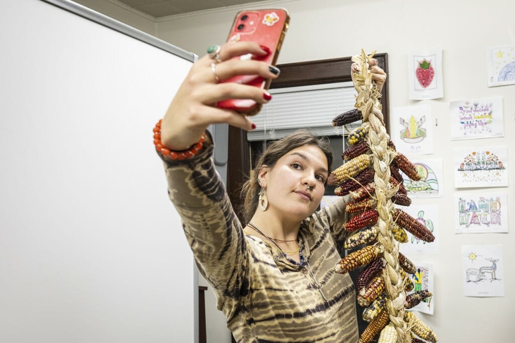 A woman holds up a phone to take a photo of her with her corn braid.