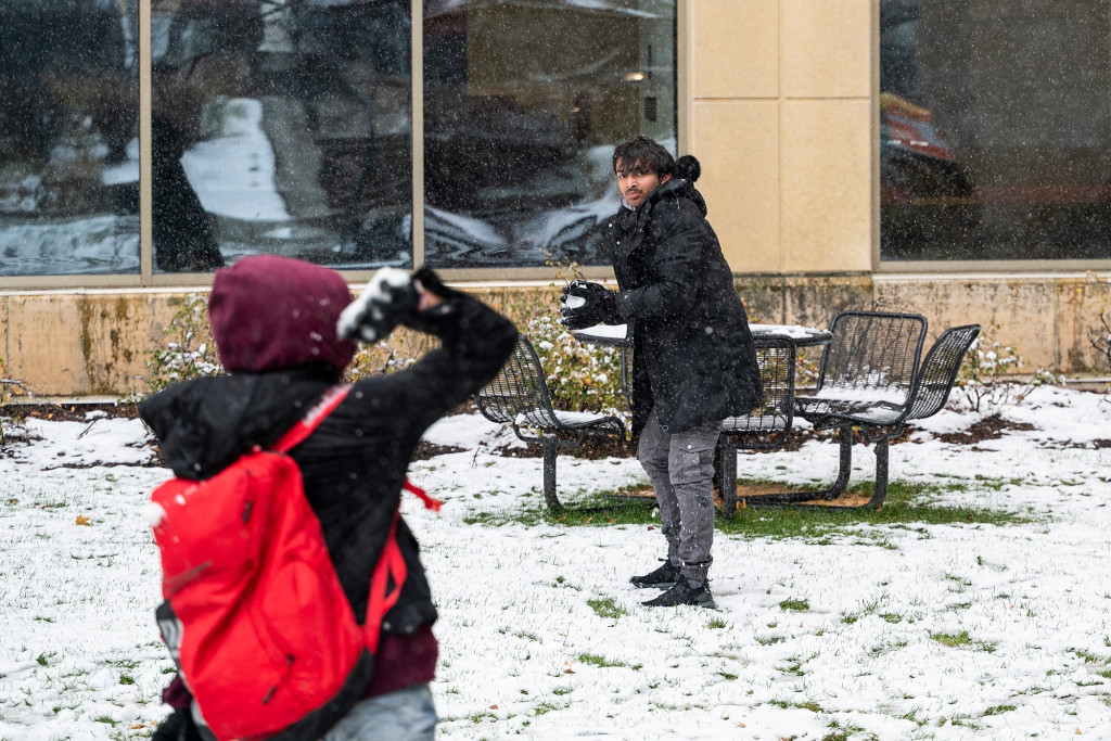 Two people throw snowballs at each other.