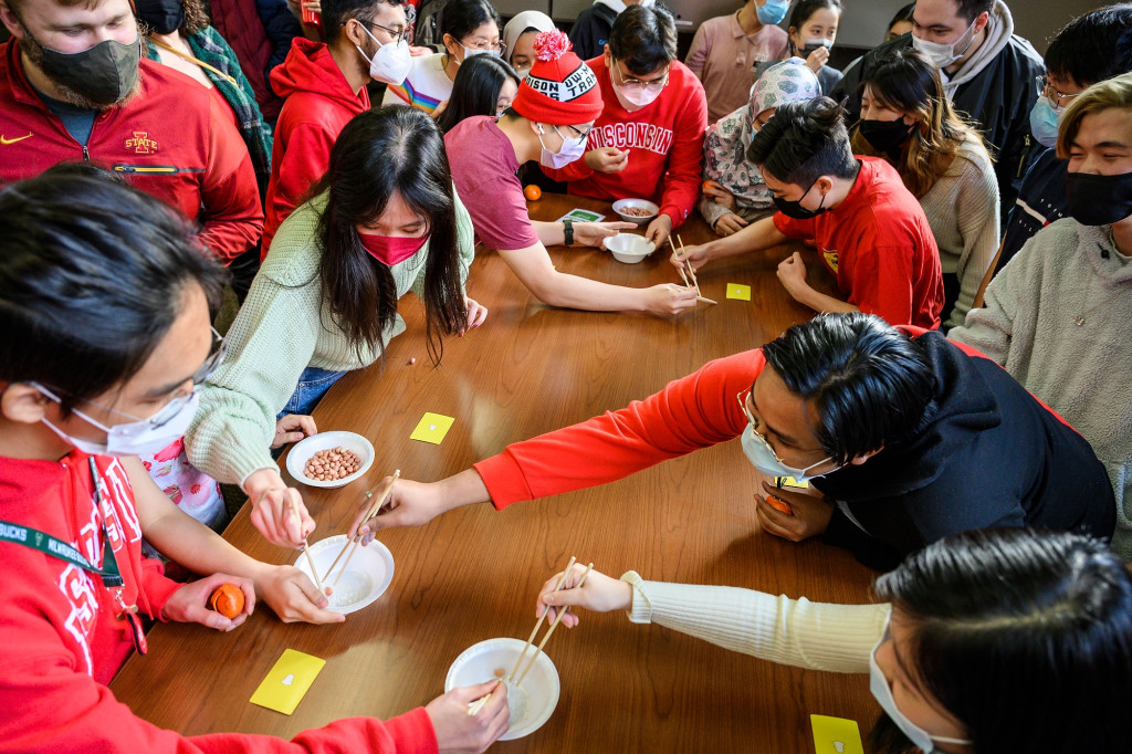 A view from above of students crowded around a table in a competition to pick up a peanut from a bowl and move it to a yellow card on the table.