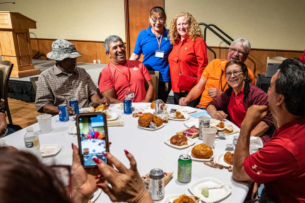 Seated at a round dining table, a group of second- and third-shift staff, including Santa Ibarra (standing) talk with Chancellor Jennifer Mnookin.